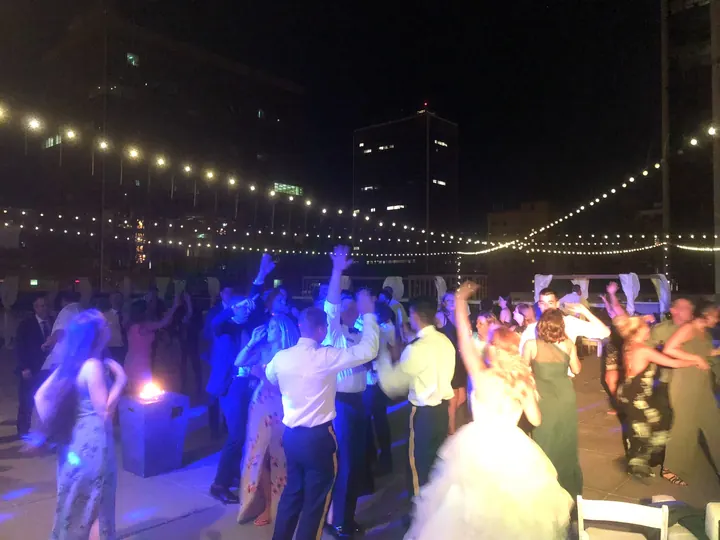 Wedding guests dancing on a rooftop beneath string lights